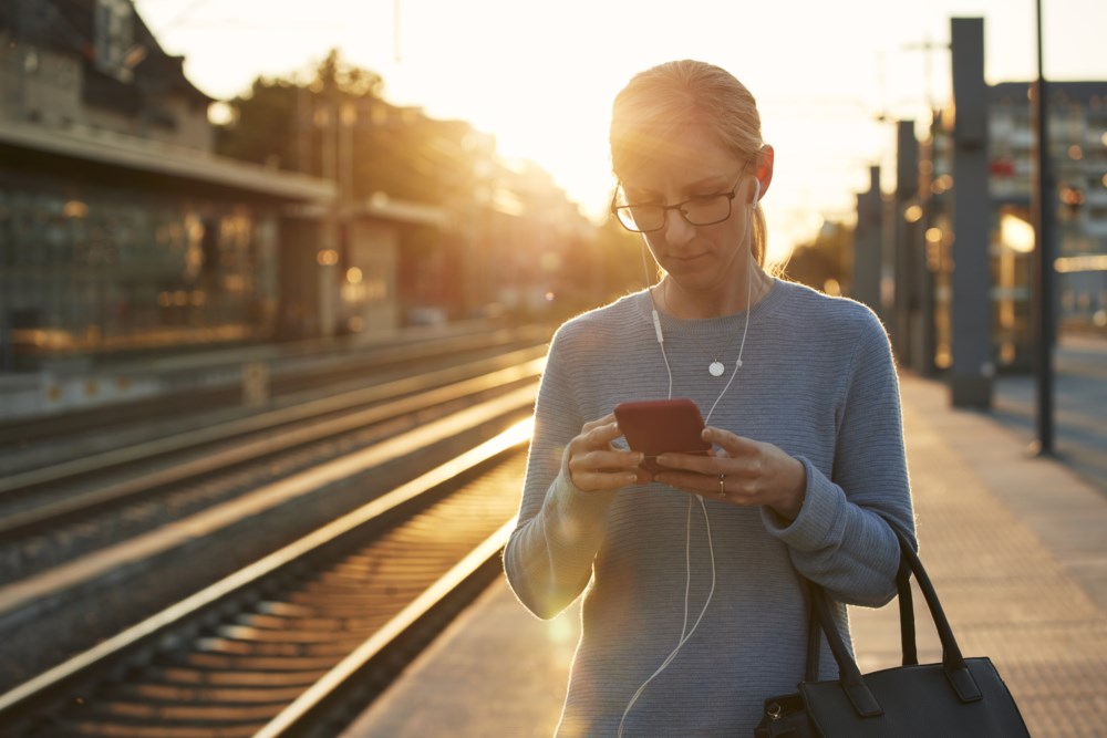 Dame på togperrong om morgenen ser på mobilen