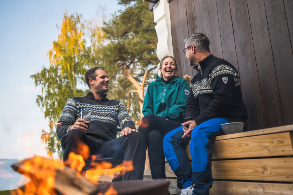 Tre mennesker sitter i hytteveggen foran et bål