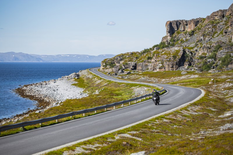 Motorsyklist kjører langs vei ved havet