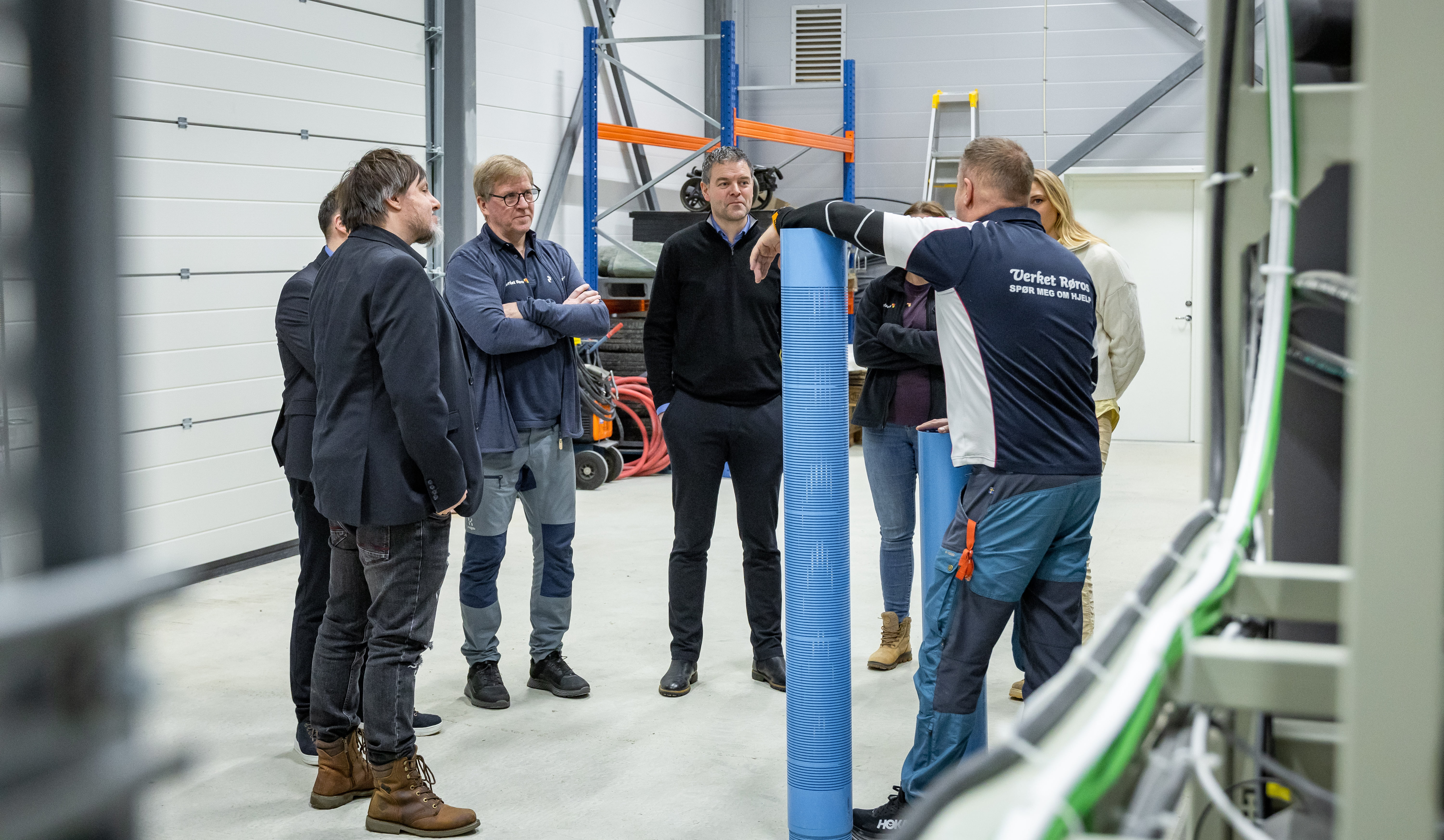 En gruppe mennesker som står og snakker sammen, inne i et lagerlokale